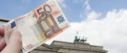 50-Euro-Schein wird vor dem Brandenburger Tor in die Luft gehalten